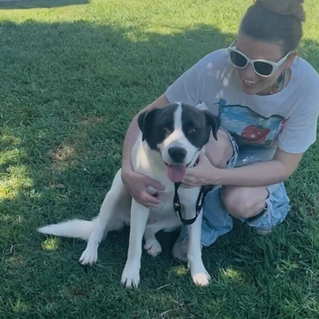 Dolly sitting beside a caregiver on the grass, with the caregiver’s arms around her.